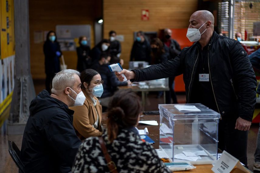Un hombre que trabaja en un centro de votación colocado en un mercado pasa un control de temperatura corporal durante las elecciones regionales en Cataluña, en Barcelona, el domingo 14 de febrero de 2021.
