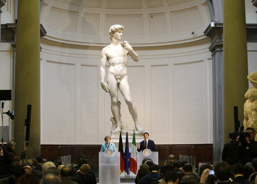 ARCHIVO. La excanciller alemana Angela Merkel y el primer ministro italiano Matteo Renzi hablan frente al David, de Miguel Ángel, en conferencia de prensa después de su reunión en Florencia, el 23 de enero de 2015. Turistas visitan la Galleria dellAccademia de Florencia, que alberga la escultura.