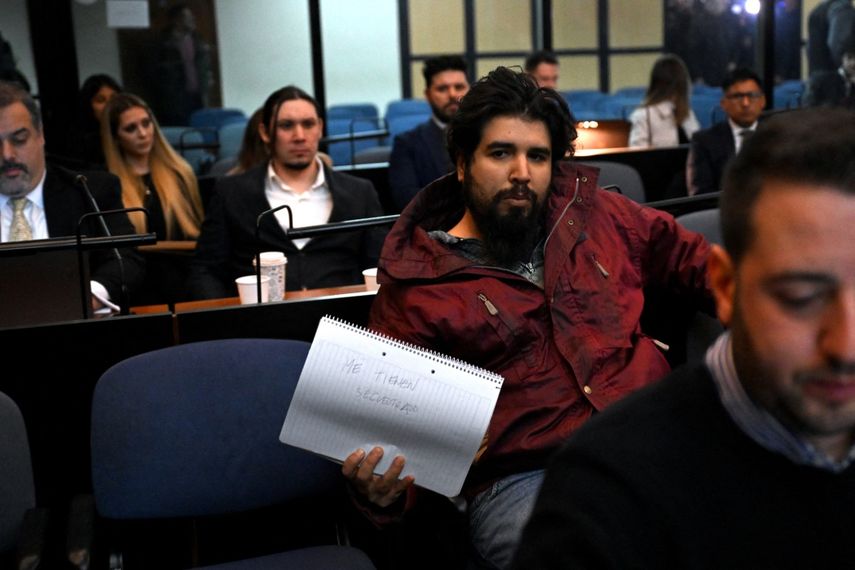 Fernando Sabag Montiel (2º-R), uno de los imputados por el intento de asesinato de la exvicepresidenta argentina Cristina Fernández de Kirchner, muestra una libreta que dice Me tienen como rehén durante el juicio en el juzgado de Comodoro Py, en Buenos Aires.