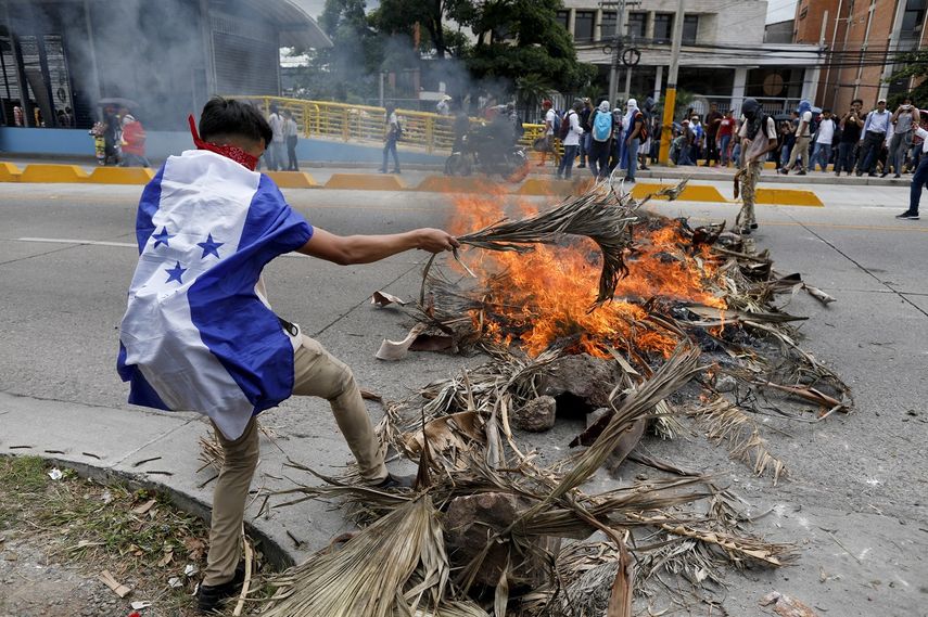 Un manifestante que usa la bandera hondureña como capa aviva el fuego durante una protesta en Tegucigalpa, Honduras, el martes 6 de agosto de 2019.