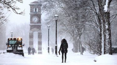 ARCHIVO - Estudiantes caminan en el campus de la Universidad de Wisconsin en La Crosse mientras un miembro del personal, a la izquierda, limpia la nieve durante una tormenta.&nbsp;