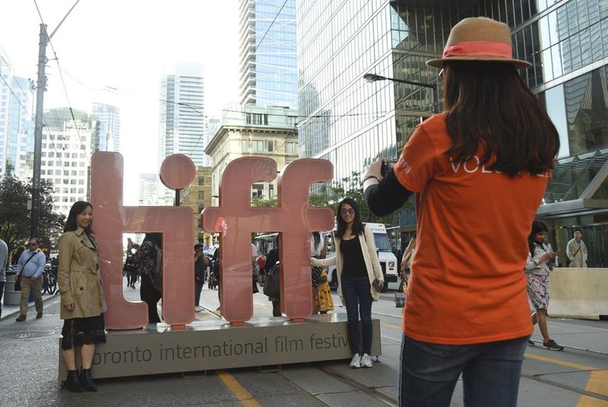 En esta fotograf&iacute;a del 5 de septiembre de 2019, un voluntario toma una foto a dos personas junto a una reproducci&oacute;n del logotipo del Festival Internacional de Cine de Toronto.