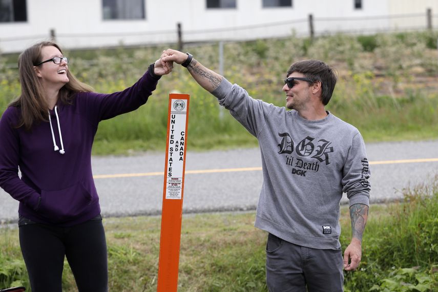 Kris Browning (izq) y su esposo Tim Browning se dan la mano por sobre un poste que marca el l&iacute;mite entre EEUU y Cand&aacute; cerca de Lynden, Washington, el 17 de mayo del 2020.