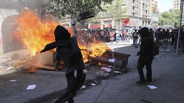 Un manifestante antigubernamental arroja un retrato del presidente Sebasti&aacute;n Pi&ntilde;era a una barricada en llamas en Santiago, Chile, el martes 22 de octubre de 2019.
