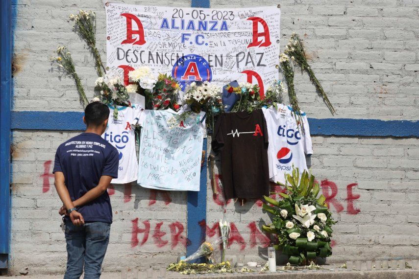 Un aficionado del Alianza se ve parado ante las ofrendas colocadas en memoria de aficionados muertos en una estampida en el estadio Cuscatlán ante el estadio, en San Salvador, El Salvador, el lunes 22 de mayo de 2023.