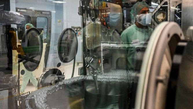 Un técnico de laboratorio, cuyo reflejo puede verse (Arriba a la derecha) supervisa las pruebas de llenado y envasado para la producción y suministro a gran escala de la vacuna candidata COVID-19 de la Universidad de Oxford, AZD1222, el 11 de septiembre de 2020 en una planta de fabricación de productos biológicos de la corporación multinacional Catalent en Anagni, al sureste de Roma, Italia.