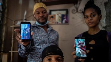 Odlanier Santiago Rodríguez, al centro, quien fue acusado de participar en las protestas de julio del año pasado y fue liberado tras 22 días en prisión, posa para una fotografía junto con su tío Emilio Román, a la izquierda, y la nuera de éste, María Carla Milán Ramos, mientras muestran fotos de los tres hijos de Román que aún permanecen detenidos. La imagen fue tomada en el barrio La Güinera en La Habana, Cuba, el miércoles 19 de enero de 2022