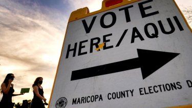 Dos votantes entregan su papeleta en una casilla electoral, el 3 de noviembre de 2020, en Tempe, Arizona.
