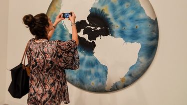 Una amante del arte toma una foto de una obra que muestra el globo del mundo durante la inauguración Art Basel en Miami Beach. (EFE)
