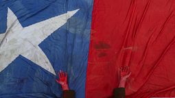 Una int&eacute;rprete coloca las manos, manchadas de pintura roja para representar sangre, sobre la bandera chilena en honor de los manifestantes muertos en los d&iacute;as de protestas reclamando mejores salarios, pensiones, escuelas, vivienda y sanidad, entre otras demandas, durante un concierto contra el gobierno en Santiago de Chile, el domingo 27 de octubre de 2019.&nbsp;
