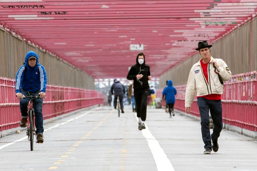 En esta foto del 11 de mayo de 2020, un hombre con mascarilla trota entre un ciclista y un peat&oacute;n que no la usan, en el puente Williamsburg de Nueva York.