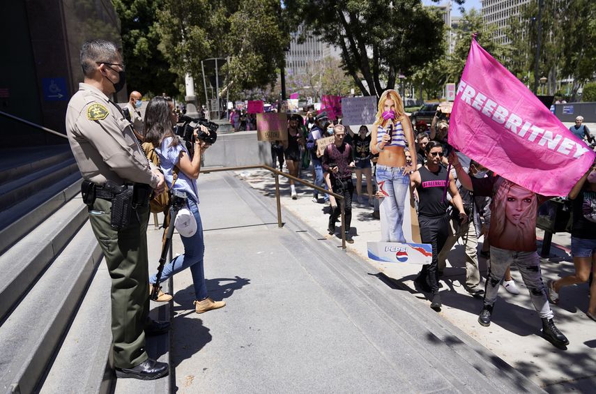 Un agente del condado de Los Angeles observa a partidarios de Britney Spears marchando frente al Palacio de Justicia Stanley Mosk durante una audiencia judicial sobre la tutela de la estrella pop, el miércoles 23 de junio de 2021 en Los Angeles.
