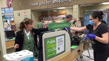 Una cajera de Publix mantiene distancia para protegerse, detr&aacute;s de una plancha de pl&aacute;stico.
