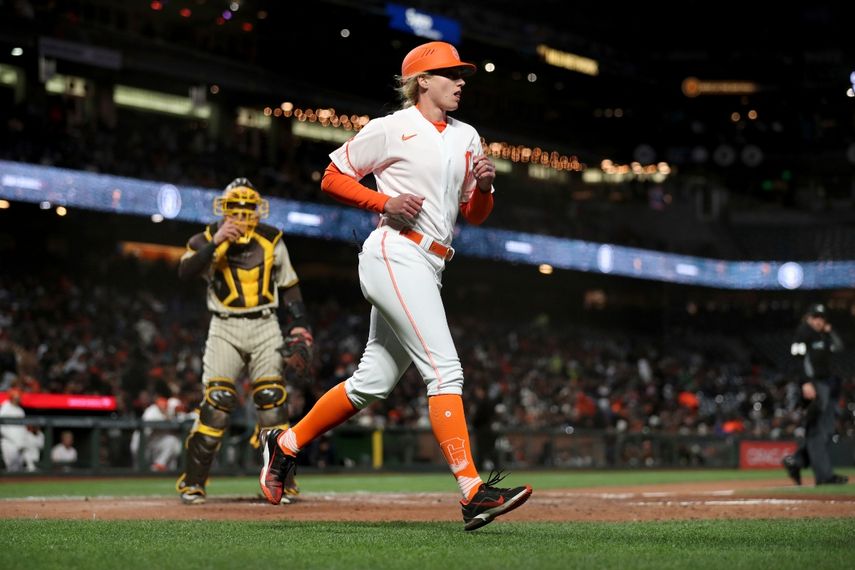 La entrenadora de primera base de los Gigantes de San Francisco Alyssa Nakken corre a su posición, cerca del catcher de los Padres de San Diego Austin Nola (izquierda), en el tercer inning del juego de la MLB que enfrentó a ambos equipos, en San Francisco