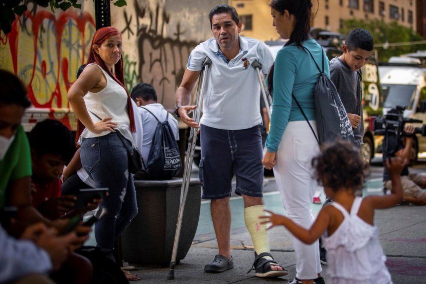 El migrante Eduardo García de pie con muletas, y rodeado de su familia afuera de la sede de Caridades Católicas, en Nueva York. 