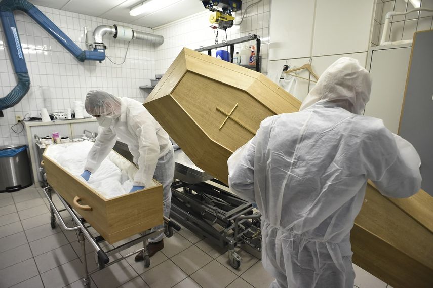 Personal sanitario arregla una urna para sacar a un fallecido de un hospital en Italia.