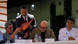 Alias Pablo Beltrán, de la guerrilla colombiana Ejército de Liberación Nacional (ELN), recibe documentos para firmar junto al miembro del ELN Antonio García, en el centro, mientras se sientan con el representante del gobierno colombiano Iván Danilo Rueda durante una ceremonia de firma acordando reanudar el diálogo de paz en la Casa Cultural Aquiles Nazoa en Caracas, Venezuela.