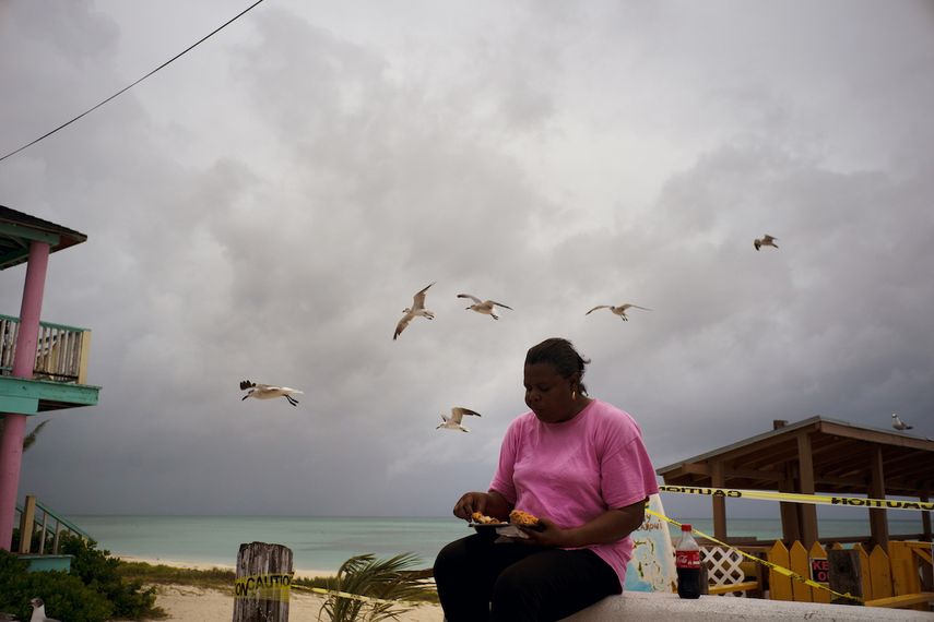 Gaviotas vuelan cerca de una mujer que las alimenta al acumularse nubes negras y acercarse el huracán Dorian en la playa Taino en Freeport, Gran Bahama, Bahamas, el domingo 1 de septiembre de 2019.&nbsp; &nbsp;