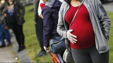 En esta fotografía de archivo del jueves 7 de mayo de 2020, una mujer embarazada que utiliza mascarilla y guantes por la pandemia de coronavirus hace fila con numerosas personas para recibir una despensa de alimentos financiada por la organización caritativa Healthy Waltham en la iglesia St. Mary en Waltham, Massachusetts.