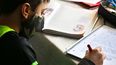 Un niño realiza sus tareas escolares mientras usa una mascarilla contra el COVID-19.