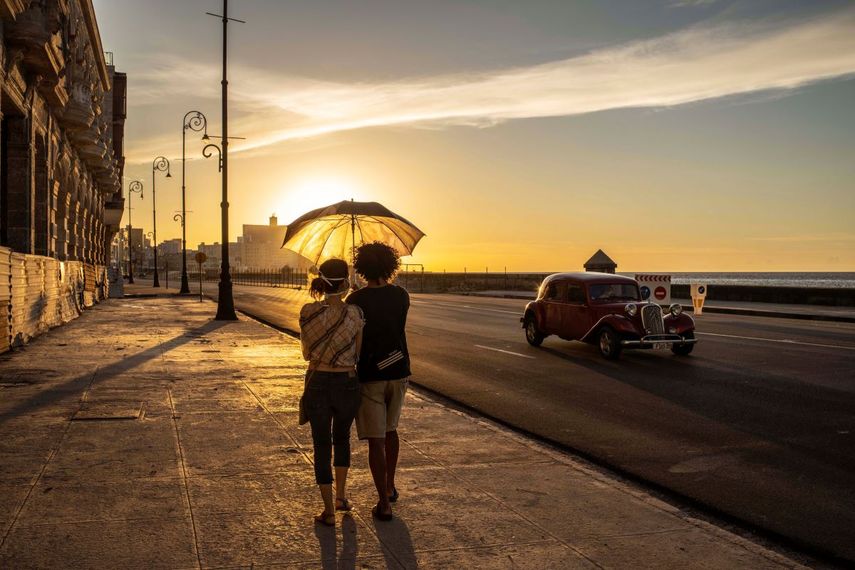 Una pareja con mascarillas para protegerse del nuevo coronavirus sostiene un paraguas mientras camina por el malecón al atardecer en La Habana, Cuba, el lunes 31 de agosto de 2020. Las autoridades de La Habana dispusieron prorrogar la noche del viernes un paquete de medidas restrictivas que incluyen el toque de queda nocturno en la capital mientras tratan de controlar un rebrote de COVID-19.