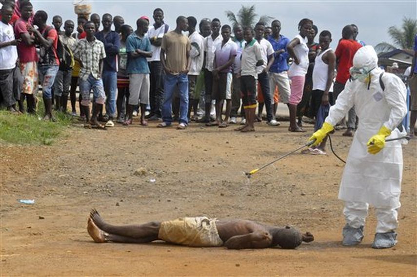 Un trabajador médico, a la derecha, rocía con químicos desinfectantes el cadáver de un hombre que se sospecha murió enfermo de ébola mientras otras personas observan. (Foto AP)