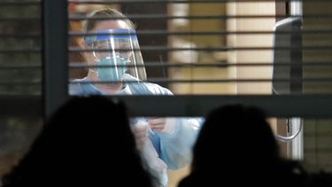 Una trabajadora vestida con una máscara y un traje de protección, vista a través de una ventana en el interior de la habitación de Susan Hailey, de 76 años, quien dio positivo por un nuevo coronavirus, mientras las hijas de la paciente observan desde fuera, el 10 de marzo de 2020, en el Life Care Center en Kirkland, Washington, cerca de Seattle, EEUU. 