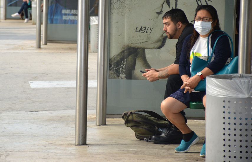 Una mujer aguarda por el autobús en Miami, mientras se protege con una mascarilla.
