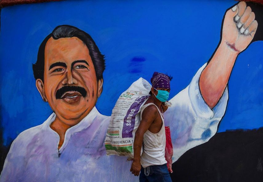 Un desamparado usa una m&aacute;scara facial para protegerse del nuevo coronavirus, COVID-19, mientras camina junto a un mural con la imagen del dictador nicarag&uuml;ense Daniel Ortega, en Managua el 9 de abril de 2020.