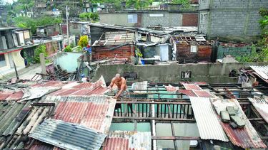 Un hombre trata de colocar láminas de metal para hacer el techo de su vivienda.