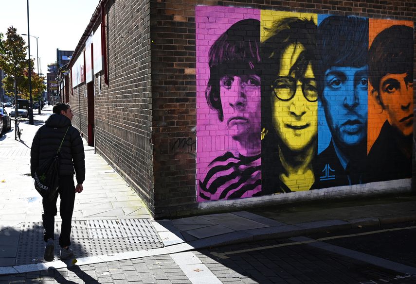 Los peatones pasan por un mural que representa a los miembros de la banda de rock británica The Beatles: Ringo Starr, John Lennon, Paul McCartney y George Harrison en el costado de un edificio en Liverpool, noroeste de Inglaterra, el 13 de octubre de 2020.