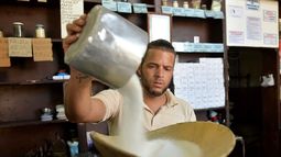 Azúcar, un empleado de tienda deposita el preciado producto en una pesa, Cuba.