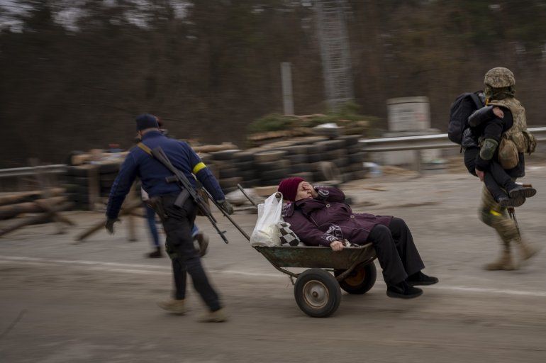 Un soldado ucraniano y un miliciano ayudan a una familia que huye a cruzar el río Irpin en las afueras de Kiev, Ucrania, el sábado 5 de marzo de 2022. 