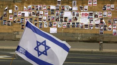 La bandera israelí está colocada cerca de una pared repleta de imágenes de rehenes israelíes arrebatados por el grupo militante palestino Hamás la semana pasada en un ataque sorpresa a Israel, frente al Ministerio de Defensa en Tel Aviv el 16 de octubre de 2023.&nbsp; &nbsp;