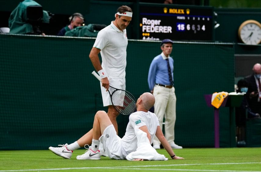 Roger Federer charla con Adrian Mannarino tras la lesión sufrida por este en el duelo de primera ronda del torneo de Wimbledon, el martes 29 de junio de 2021, en Londres