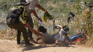 Los migrantes que cruzan a Estados Unidos desde México son auxiliados a pasar debajo de alambre de púas en una de las márgenes del río Bravo, el jueves 21 de septiembre de 2023, en Eagle Pass, Texas.