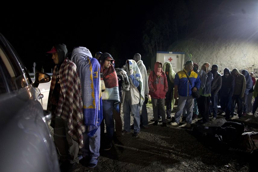 Fotograía del 31 de agosto de 2018 de un grupo de migrantes venezolanos en fila para recibir pan y café donado por una familia que les atiende desde su auto, en una gasolinera de Pamplona, Colombia.