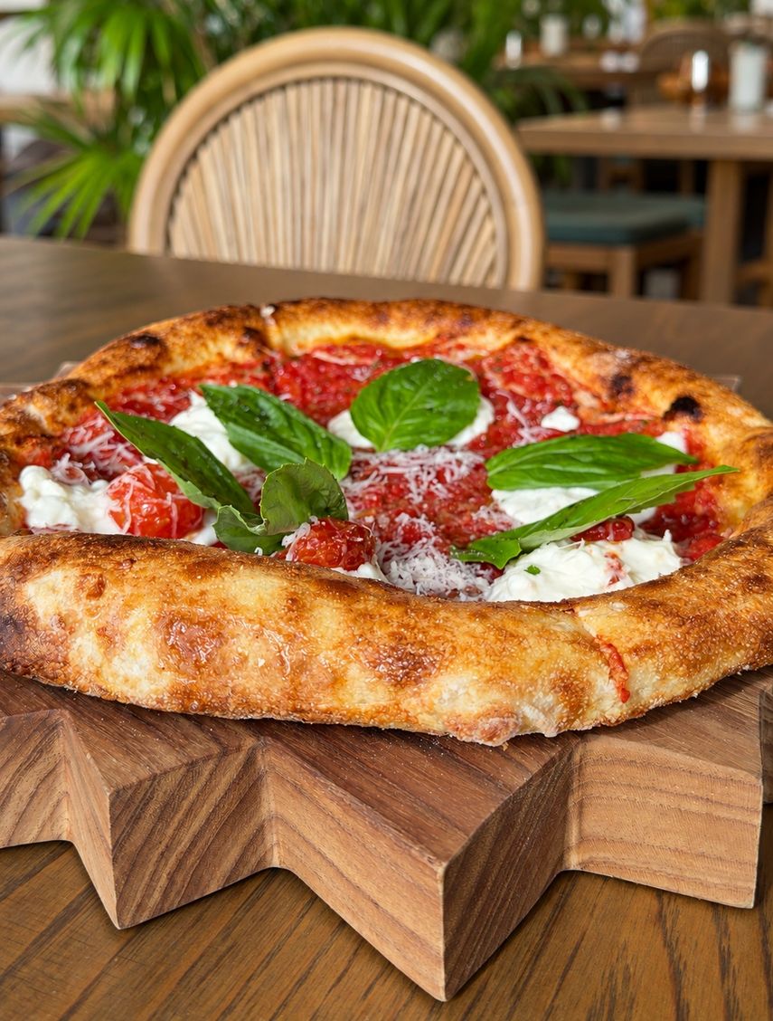 Albahaca fresca, tomate y queso destacan sobre la masa de bordes dorados.
