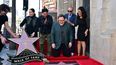 El actor estadounidense Robert Downey Jr. coloca el primer chicle en la recién inaugurada estrella del Paseo de la Fama de Hollywood de John Favreau el 13 de febrero de 2023 en Hollywood, California, mientras Favreau y el chef Roy Choi reaccionan.