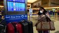 Una mujer en el aeropuerto de Los Angeles usa una mascarilla mientras busca información en la pantalla sobre su vuelo.