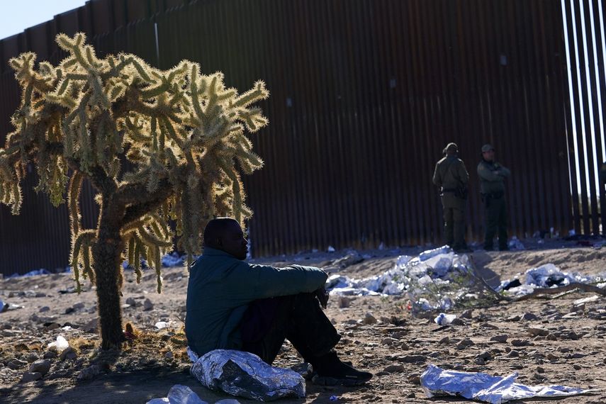 Un migrante se sienta a la sombra de un cactus saltarín del desierto mientras se une a cientos de migrantes reunidos a lo largo de la frontera, el martes 5 de diciembre de 2023 en Lukeville, Arizona.&nbsp;