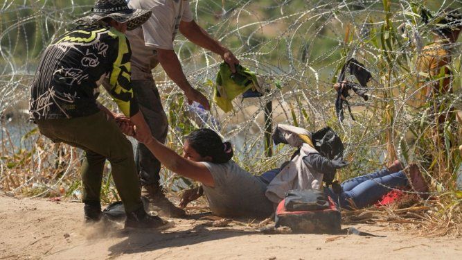 Los migrantes que cruzan a Estados Unidos desde México son auxiliados a pasar debajo de alambre de púas en una de las márgenes del río Bravo, el jueves 21 de septiembre de 2023, en Eagle Pass, Texas.