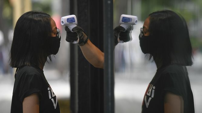 Un empleado de una tienda le toma la temperatura a una mujer como precaución contra el coronavirus el sábado 25 de julio de 2020, en Caracas, Venezuela. 