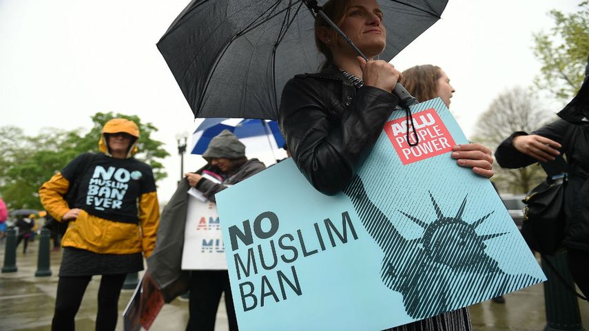 Manifestantes llevan pancartas con mensajes en contra del veto migratorio de Trump durante una concentración ante la Corte Suprema, en Washington