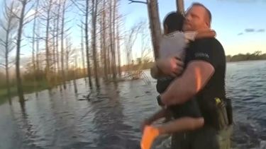 En esta imagen extraída de un video grabado con una cámara corporal de un policía del condado Volusia, Florida, el agente Wes Brough salva a un niño autista de 5 años de un estanque en Deltona, Florida.   