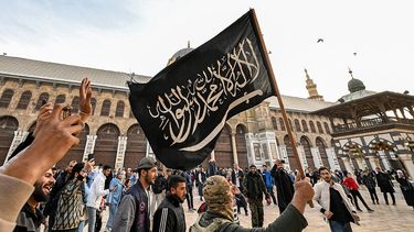Un combatiente rebelde sirio sostiene una bandera negra islamista que representa lealtad al culto musulmán, mientras camina por el patio de la Gran Mezquita de Damasco del siglo VIII.
