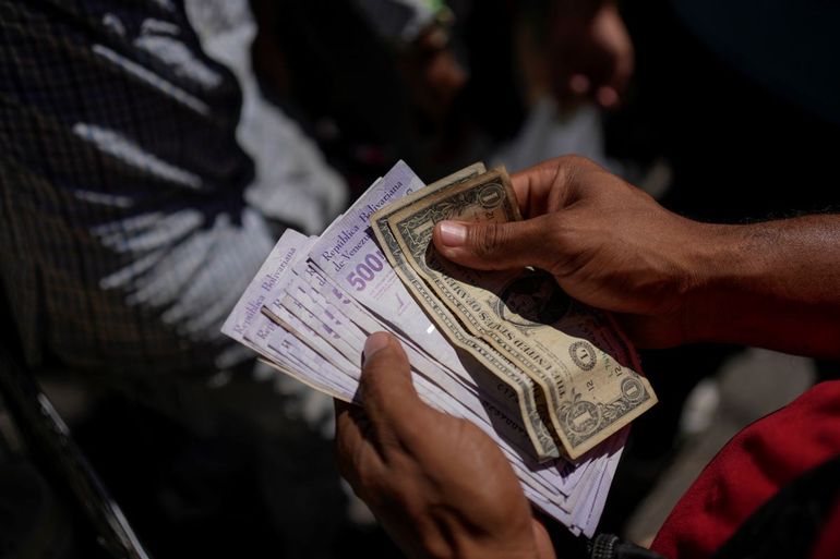 Un vendedor cuenta bolívares venezolanos y billetes de dólares estadounidenses para entregar cambio a un cliente en un mercado público en el barrio de Petare en Caracas, Venezuela, el martes 18 de enero de 2022.