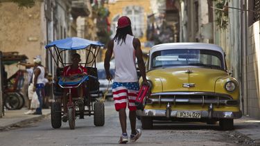 Un hombre camina cerca de un vehículo clásico y un bicitaxista en la Habana Vieja.&nbsp;