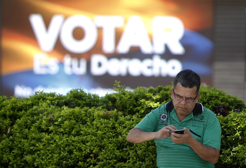 Un hombre revisa su teléfono afuera de un colegio electoral.&nbsp;