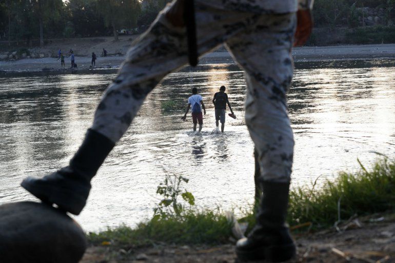 En esta fotografía del 22 de enero de 2020, unos migrantes hondureños que trataron de cruzar la frontera hacia México a pie regresan al lado guatemalteco del río Suchiate bajo la vigilancia de un elemento de la Guardia Nacional mexicana, cerca de Ciudad Hidalgo, México.